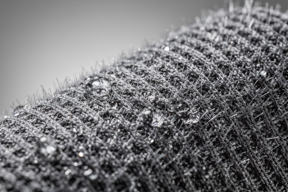 Close-up of water droplets on a gray, textured, woven fabric with small, spiky fibers.